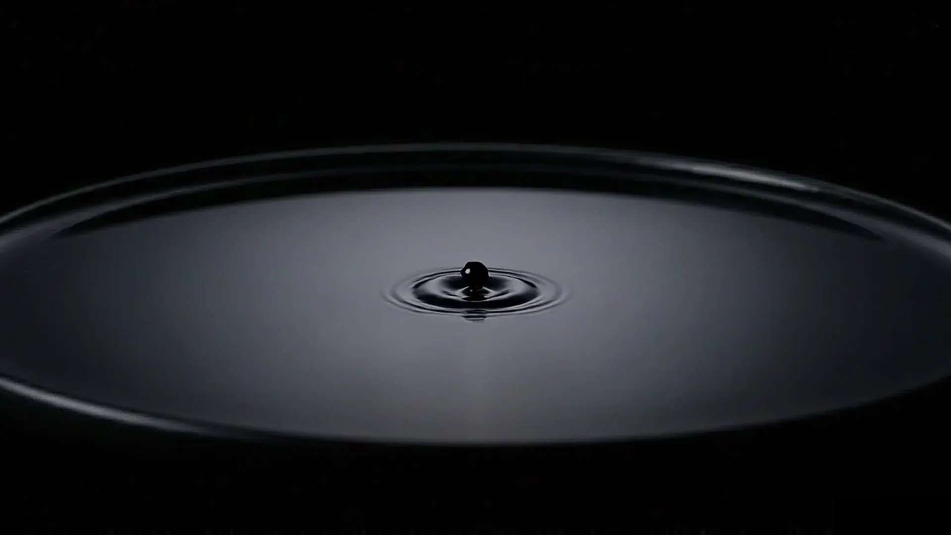 A single drop of ink about to touch still black water